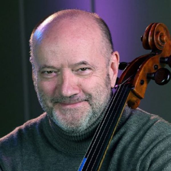 Gethyn Jones, a bald white man, holding his cello wearing a grey turtleneck