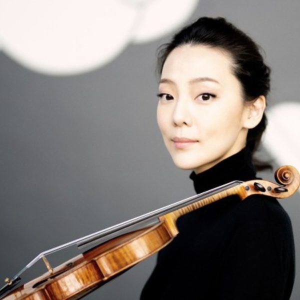 Clara Jumi Kang, an Asian woman with tied up black hair, wearing a black turtleneck and resting her violin on her left shoulder