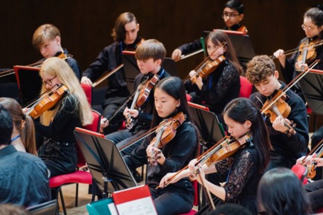 Members of the Youth Orchestra string section playing their instruments and wearing all black