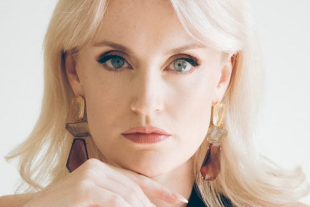 Sarah Brady, a white woman with long blonde hair, leaning on her hand looking directly at the camera