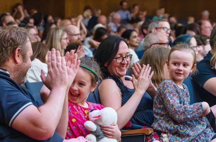 A mother, father and two young girls sat in an auditorium clapping to music