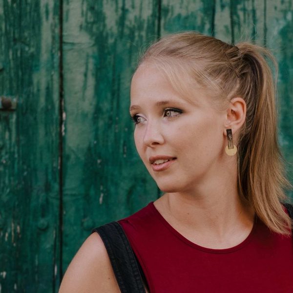 Dani Howard, a white woman with blonde hair in a ponytail, wearing a red vest and looking to the left