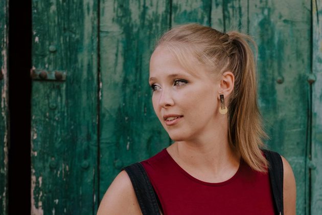 Dani Howard, a white woman with blonde hair in a ponytail, wearing a red vest and looking to the left