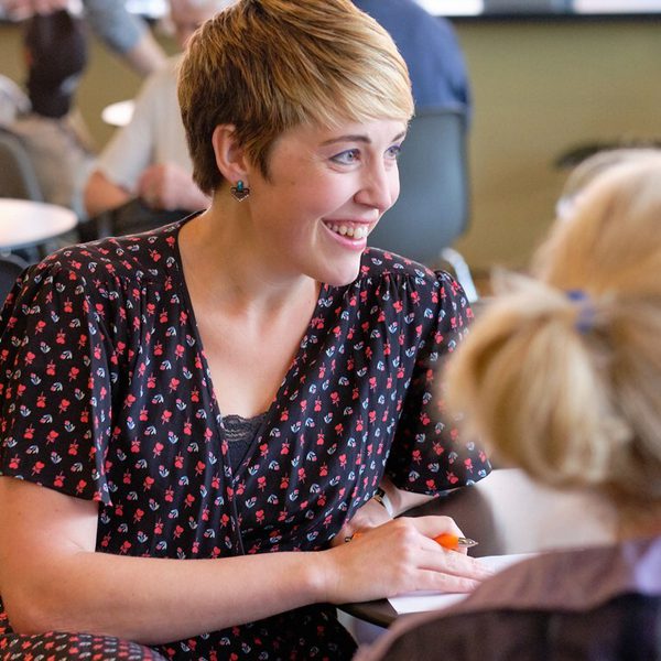 Claire Henry, a white woman with short blonde hair, wearing a polka dot dress and smiling at someone off camera