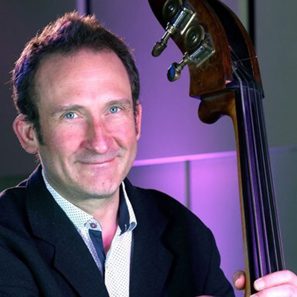 Marcel Becker, a white man with short brown hair, holding his double bass wearing a black suit