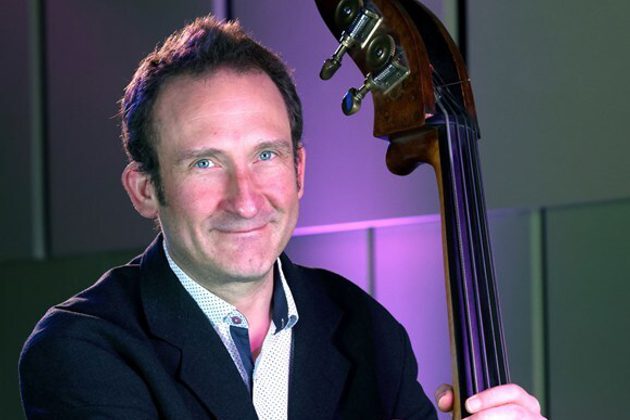 Marcel Becker, a white man with short brown hair, holding his double bass wearing a black suit