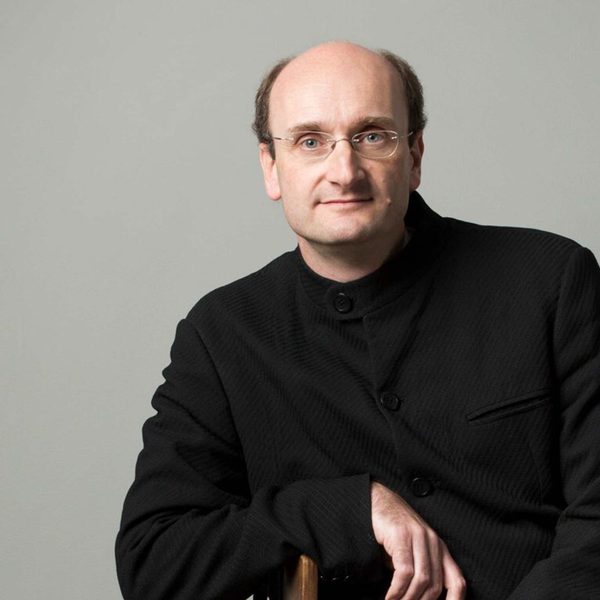 Andrew Manze, a tall white man with short black hair and glasses, sat on a chair wearing all black